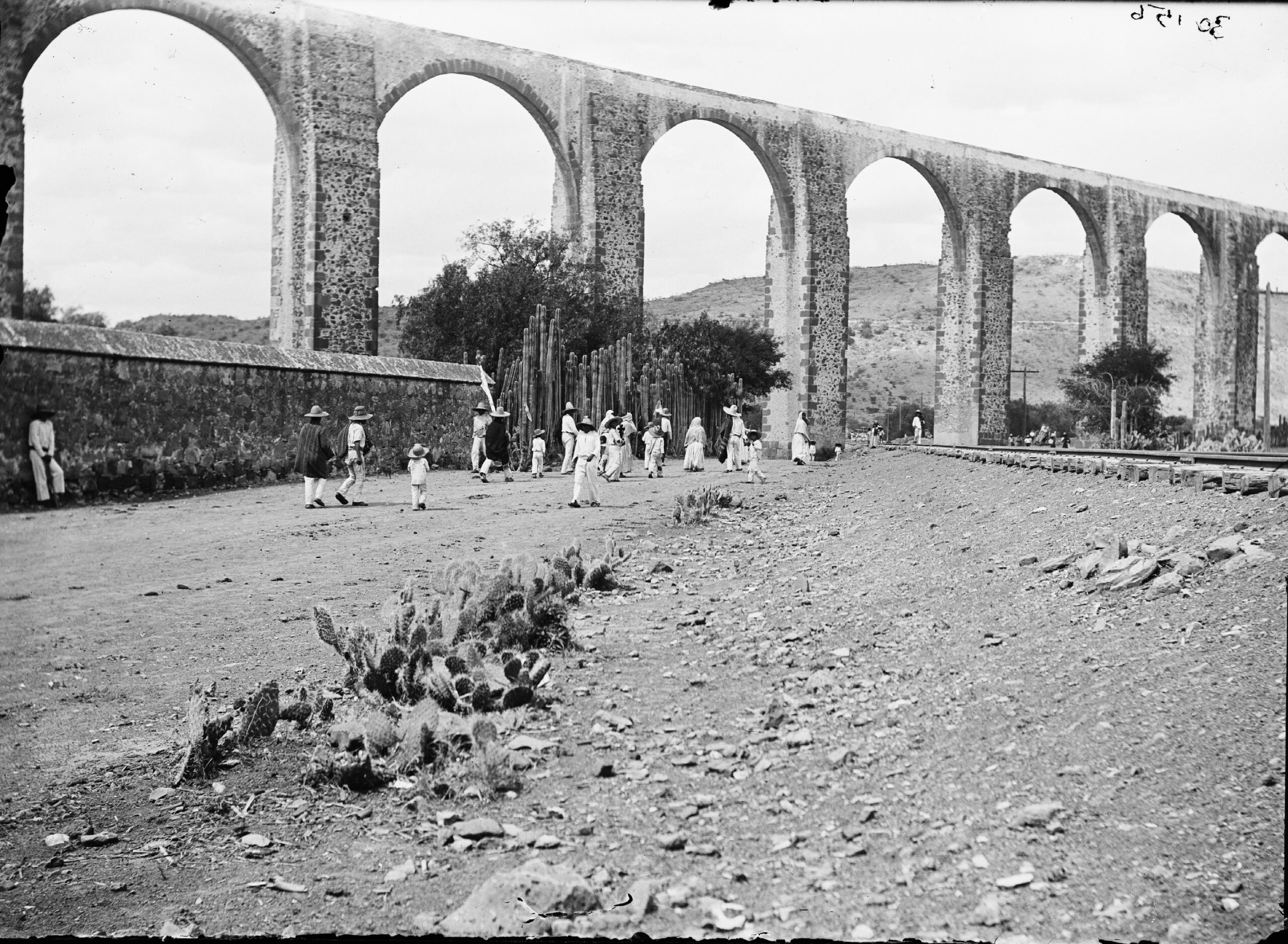 Fotografía antigua del Acueducto de Querétaro con personas vestidas con ropa tradicional mexicana, reflejando la historia y cultura de la región.