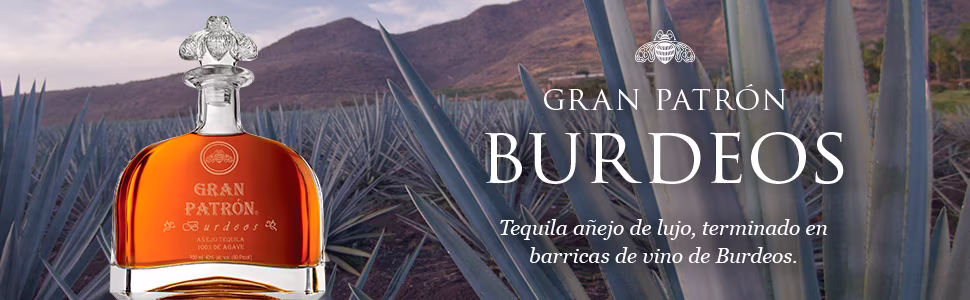Botella de Gran Patrón Burdeos, un tequila añejo de lujo terminado en barricas de vino de Burdeos, rodeada de plantas de agave azul en Jalisco, México.