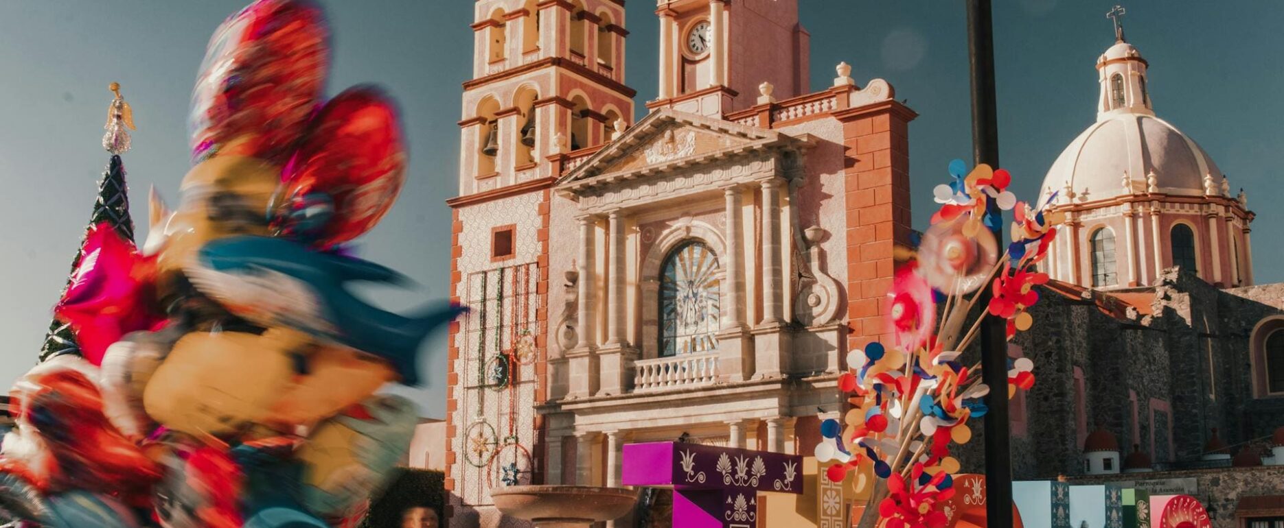 Vista de la iglesia neoclásica de Santa María de la Asunción en Tequisquiapan, uno de los Los 7 Pueblos Mágicos de Querétaro, con un vendedor de globos coloridos en primer plano.