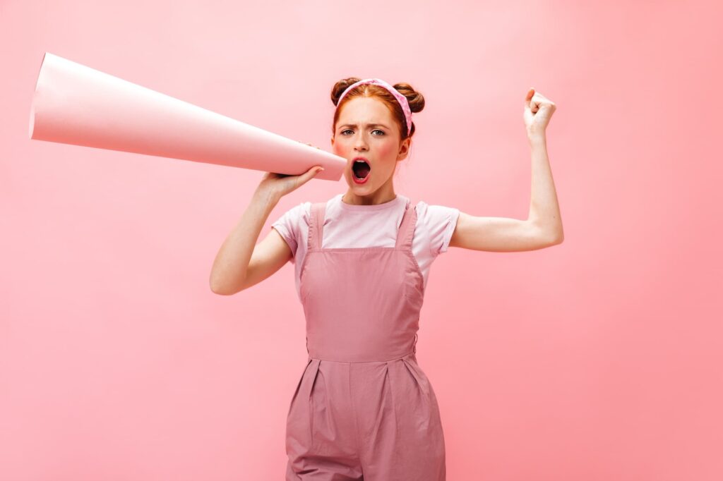 Joven con atuendo rosa sosteniendo un megáfono y expresando entusiasmo, representando estrategias de impacto y visibilidad de una agencia de marketing en Querétaro.
