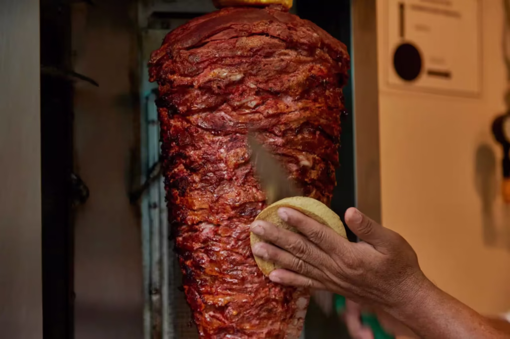 Trompo de carne al pastor girando mientras un taquero corta la carne directo sobre una tortilla recién hecha