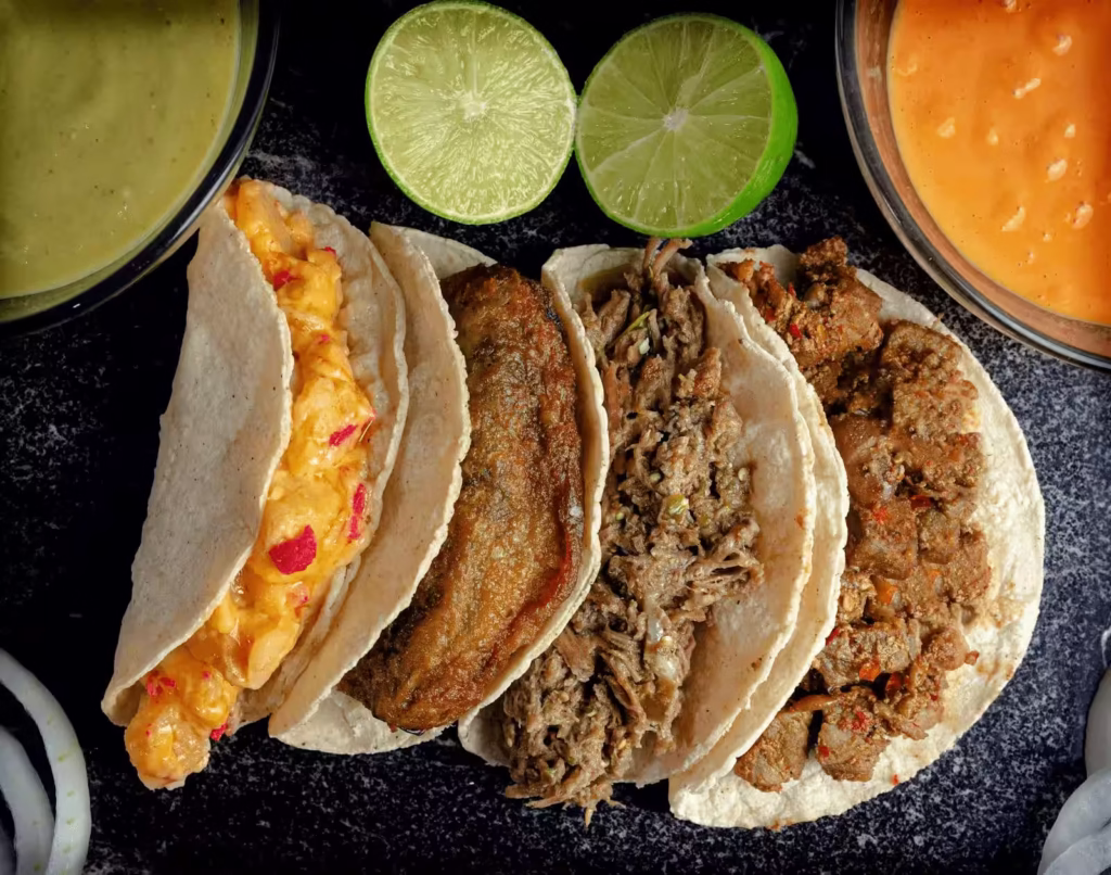 Tacos variados al estilo tradicional con salsas y cítricos Tacos gourmet con salsas mexicanas y rodajas de lima sobre tabla de madera