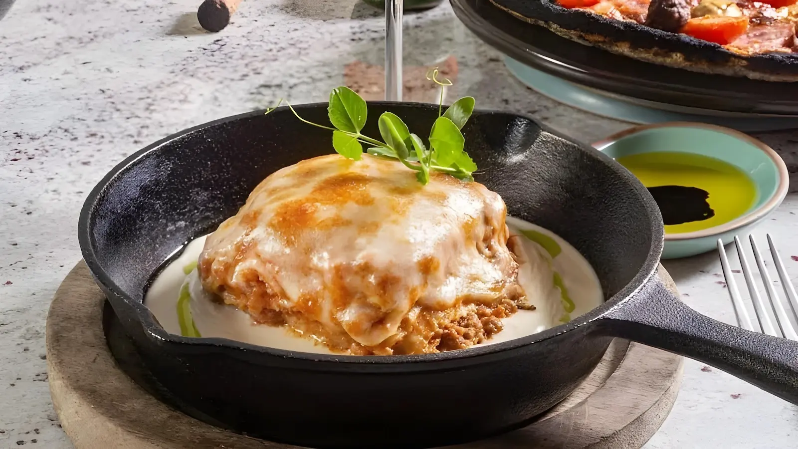 Lasaña en hierro fundido: Tradición caliente y sabor intenso en Hunger Querétaro Lasaña servida en cazuela de hierro en Hunger Juriquilla, Querétaro – comfort food artesanal con carácter y presentación de autor